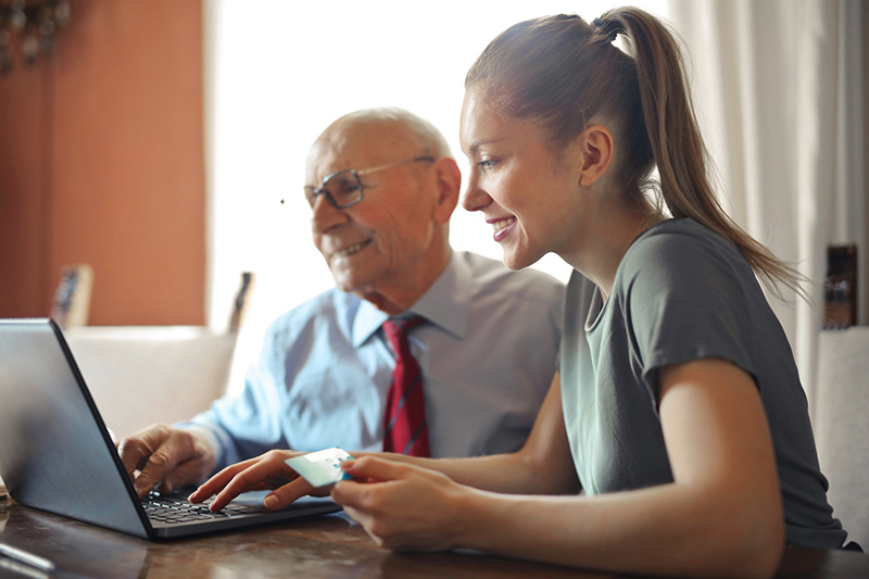 An older man and woman sit in fron of a laptop