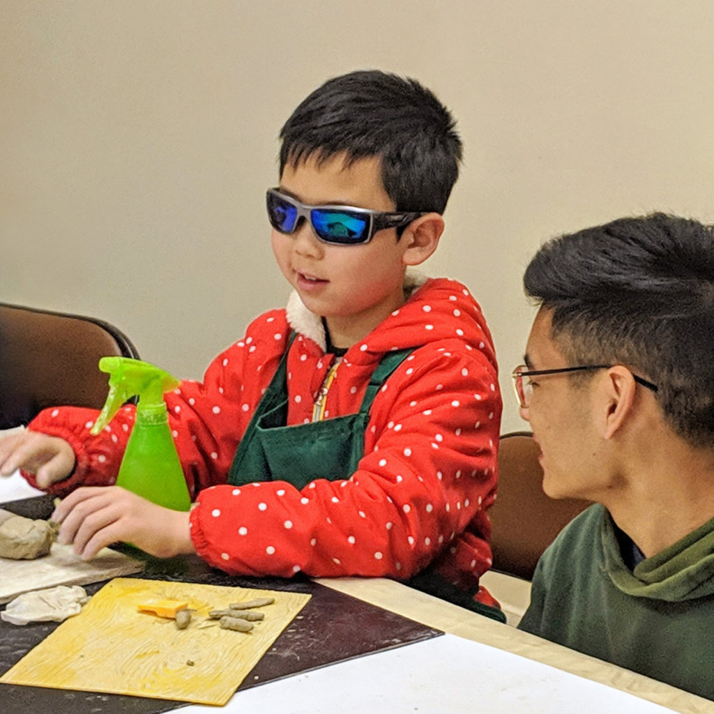 A boy with dark glasses building with clay