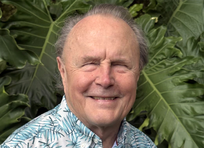 Ted Henter, the Vista Honors honoree, in front of a background of large green leaves smiling and wearing a blue, white, and green Hawaiian shirt.